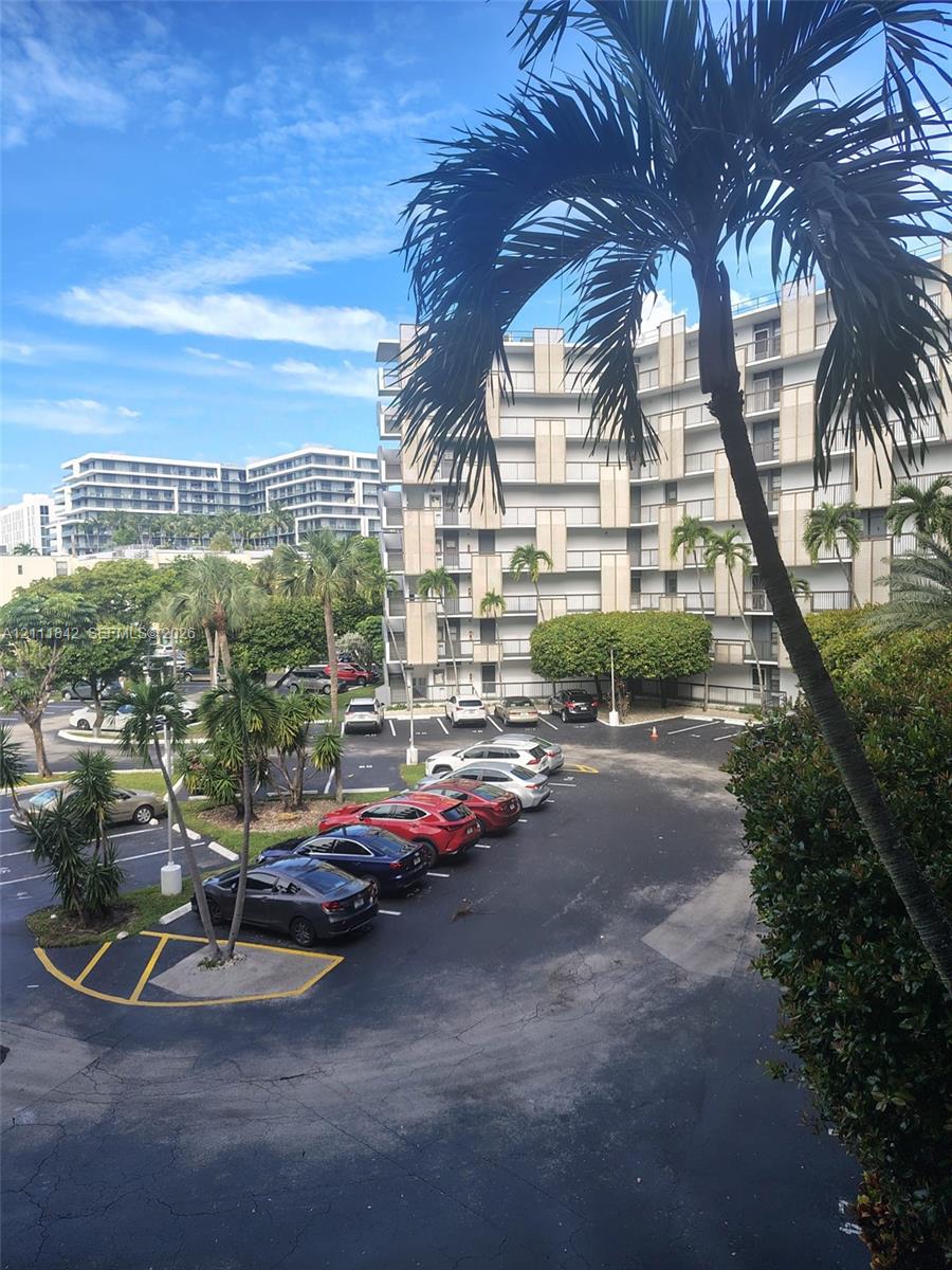 Multi-story building featuring concrete balconies, landscaped grounds with palm trees, and paved surface parking Multi-story building featuring concrete balconies, landscaped grounds with palm trees, and paved surface parking