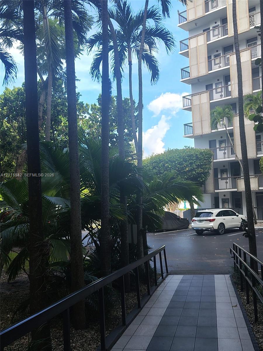 Exterior walkway featuring patterned tile paving, metal railings, and mature palm tree landscaping