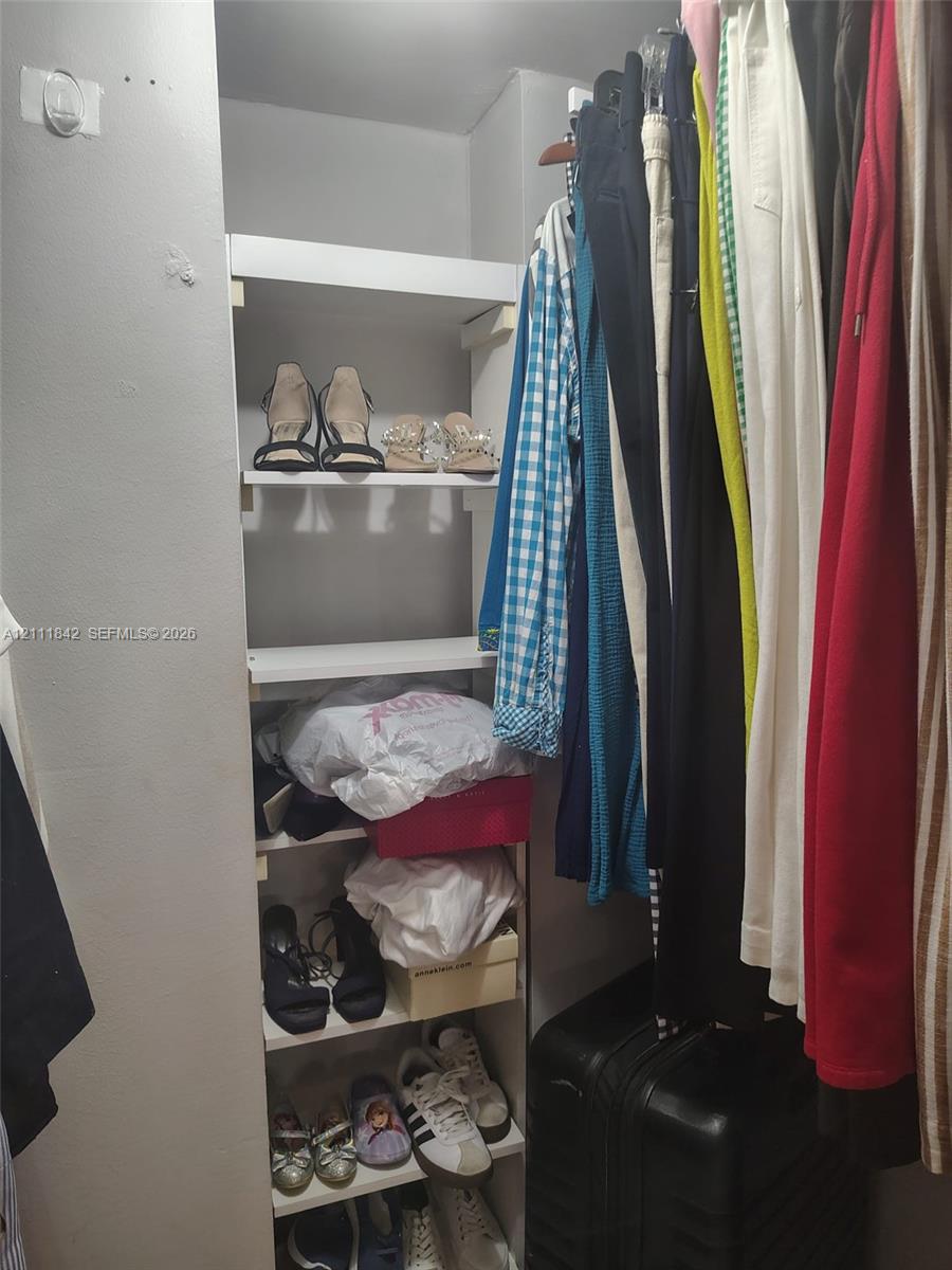 Walk-in closet featuring white built-in vertical shelving and an integrated metal garment hanging rod