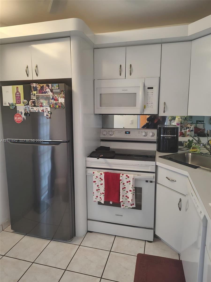 Kitchen featuring white cabinetry, stainless steel refrigerator, white electric range with over-the-range microwave, integrated mirror backsplash, and tile flooring