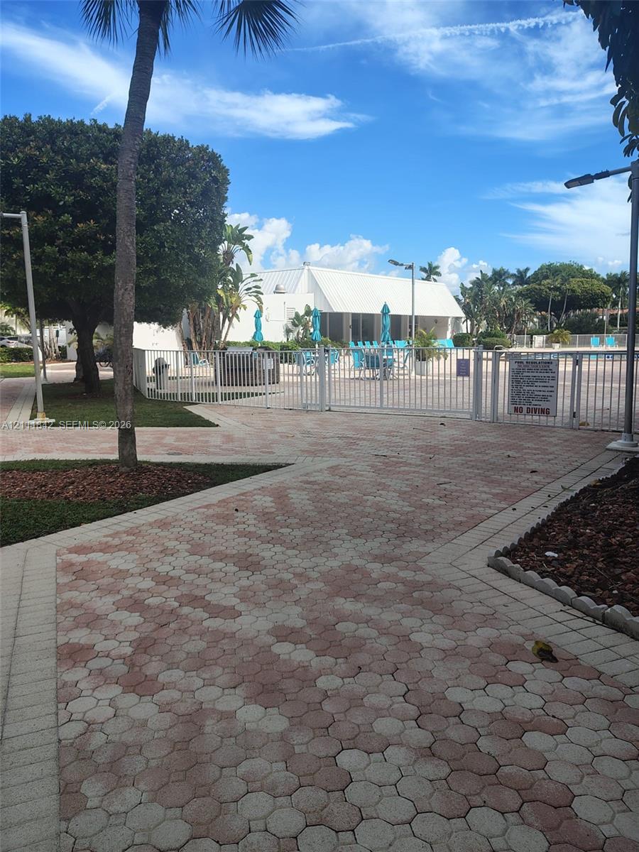 Paver walkway featuring geometric pattern masonry leading to a fenced swimming pool area with mature landscaping