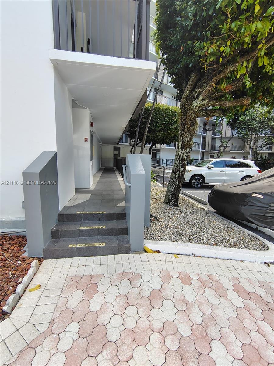 Exterior walkway featuring grey tile steps, concrete sidewalls, and a covered pedestrian path