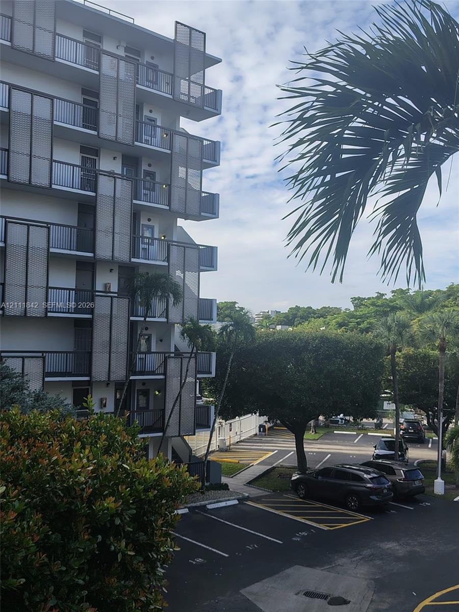 Multi-story building exterior featuring dark metal grid balcony privacy screens, private balconies, and asphalt surface parking lot