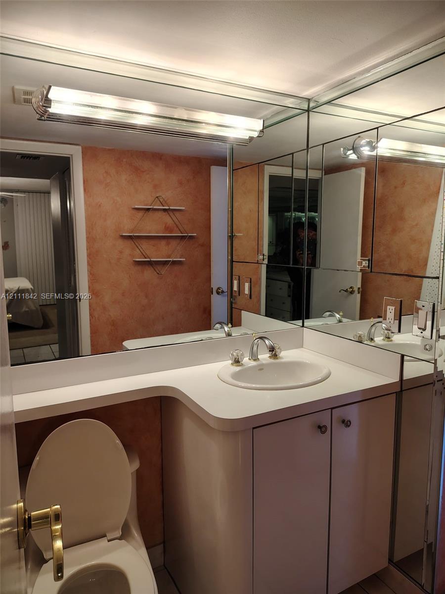 Bathroom vanity featuring a solid surface countertop, integrated sink with dual-handle faucet, white cabinetry, and a large-scale mirrored wall