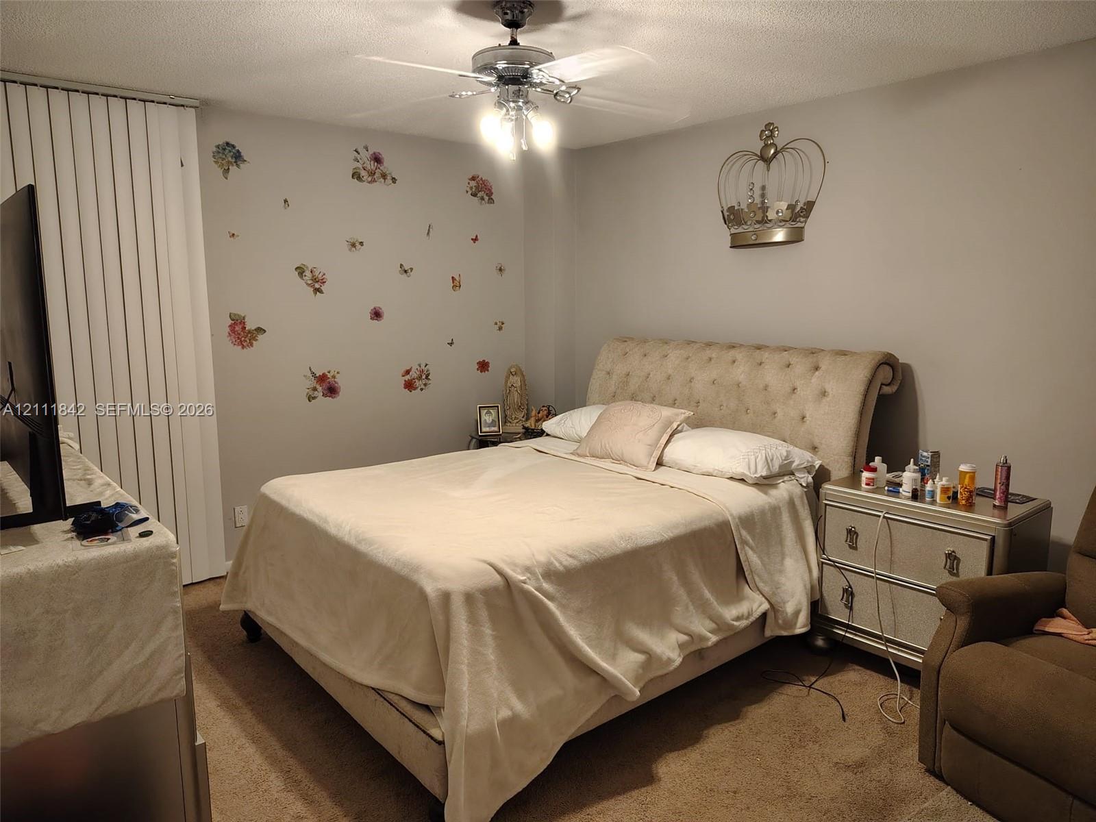 Neutral wall tones, carpeted flooring, vertical window blinds, and a central ceiling fan with multi-light fixture