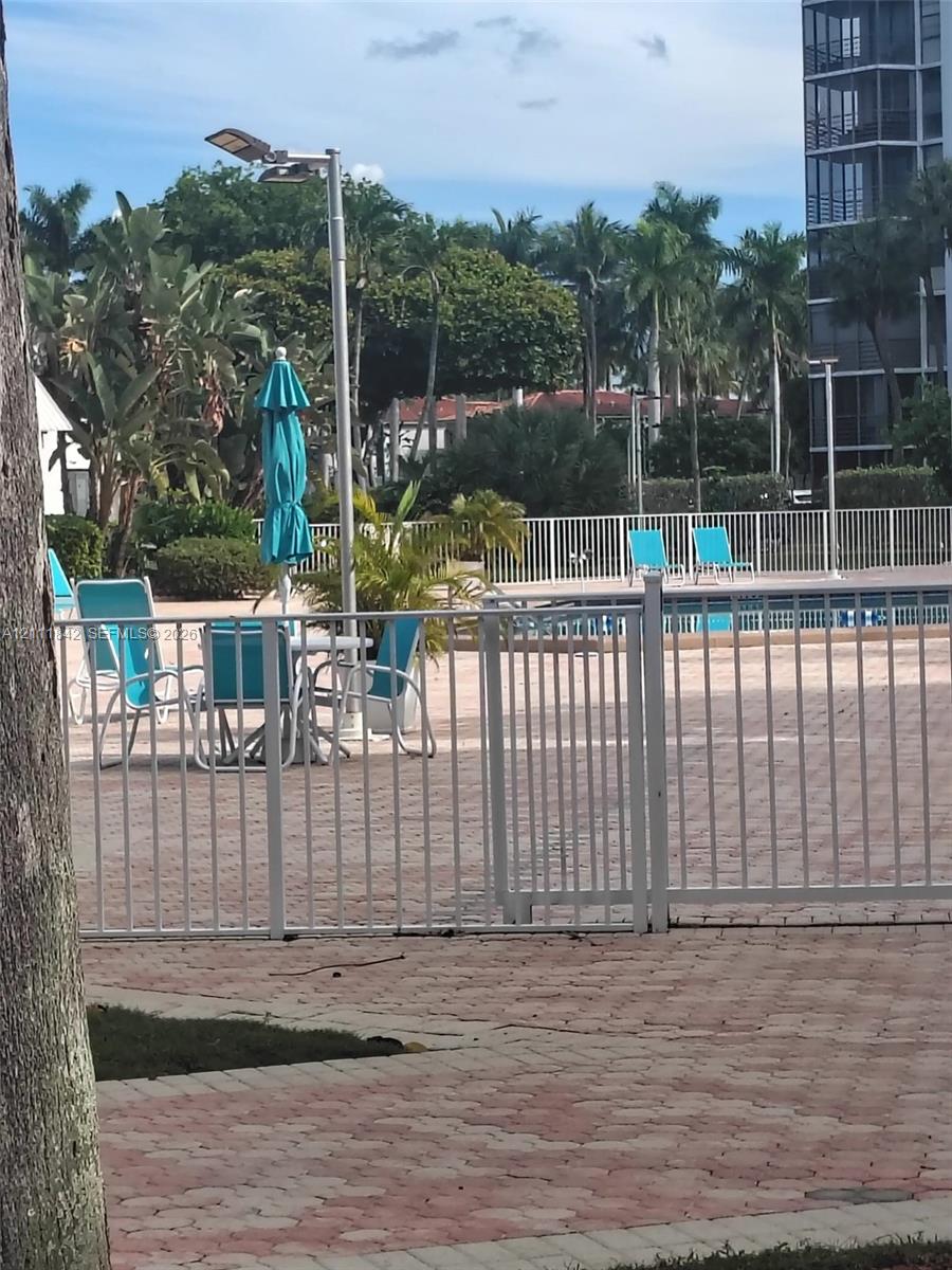 Swimming pool area featuring a paver stone deck, white metal perimeter fencing, and established palm tree landscaping
