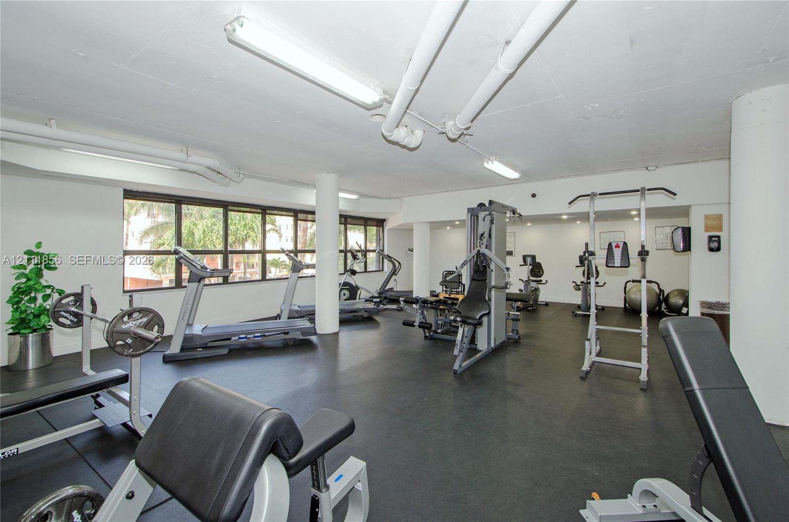 Fitness center featuring rubber flooring, expansive windows, exposed overhead infrastructure, and structural columns