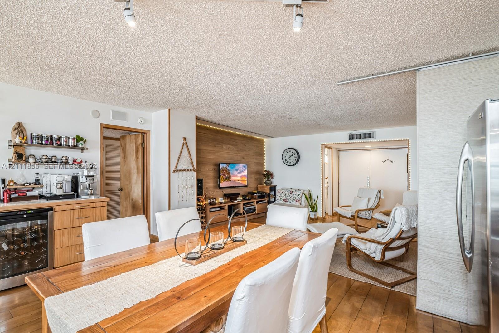 Open-concept interior featuring wood-finish flooring, a wood-paneled accent wall with integrated cove lighting, custom built-in cabinetry, and a glass-front beverage cooler