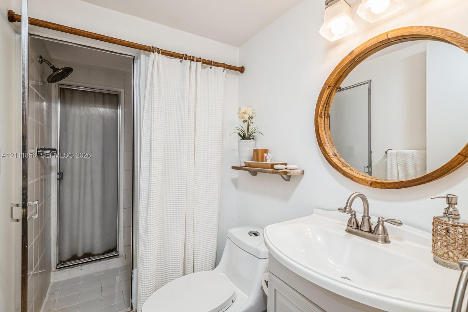 Bathroom featuring a vanity with an integrated basin, oval wood-frame mirror, wall-mounted floating shelf, and a shower enclosure with tile surround and fixed shower head