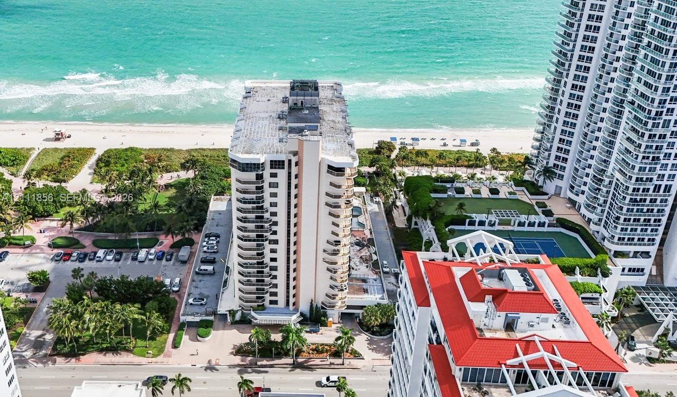 High-rise residential building featuring multiple private balconies, direct coastal frontage, paved surface parking, and shared tennis courts High-rise residential building featuring multiple private balconies, direct coastal frontage, paved surface parking, and shared tennis courts