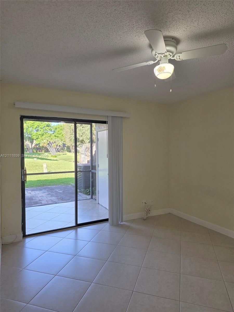Interior space featuring diagonal ceramic tile flooring, a white ceiling fan with integrated lighting, and a sliding glass door opening to a paved, screened-in patio