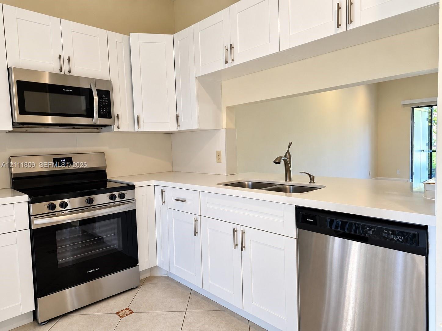Kitchen featuring white shaker-style cabinetry, solid-surface countertops, stainless steel appliances, and a double-basin undermount sink with a gooseneck faucet