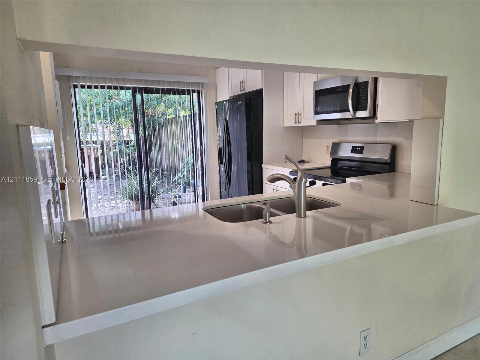 Kitchen featuring white cabinetry, solid-surface countertops, dual-basin stainless steel sink with high-arc faucet, and built-in stainless steel appliances