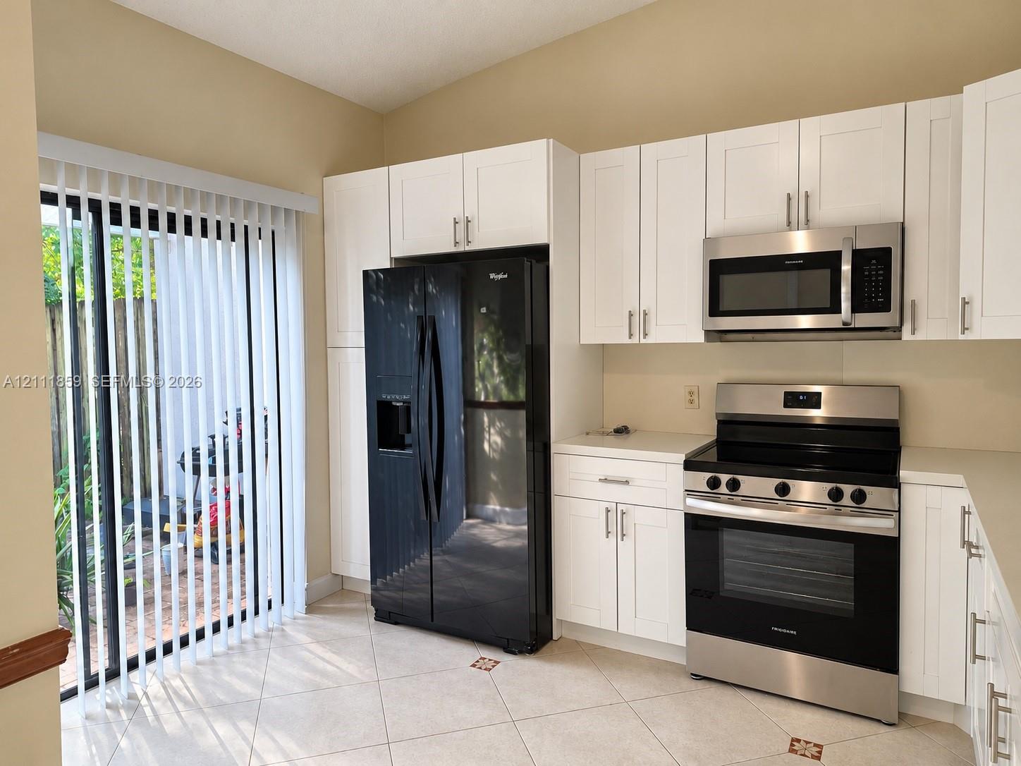 Kitchen featuring white shaker-style cabinetry, stainless steel appliance suite, black side-by-side refrigerator, solid surface countertops, and tiled flooring