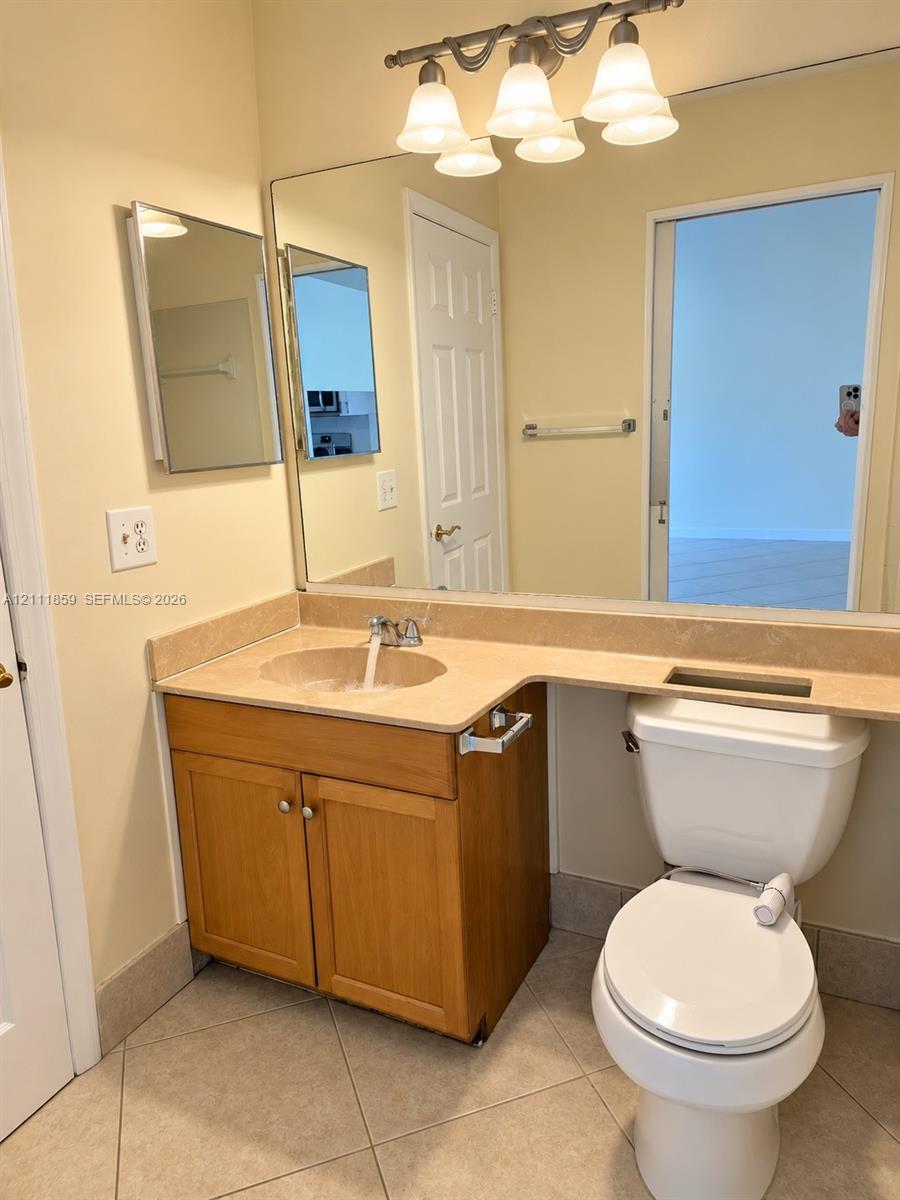 Vanity cabinet with wood-finish cabinetry, stone-surfaced countertop with integrated sink, large wall-mounted mirror, and multi-bulb fixture