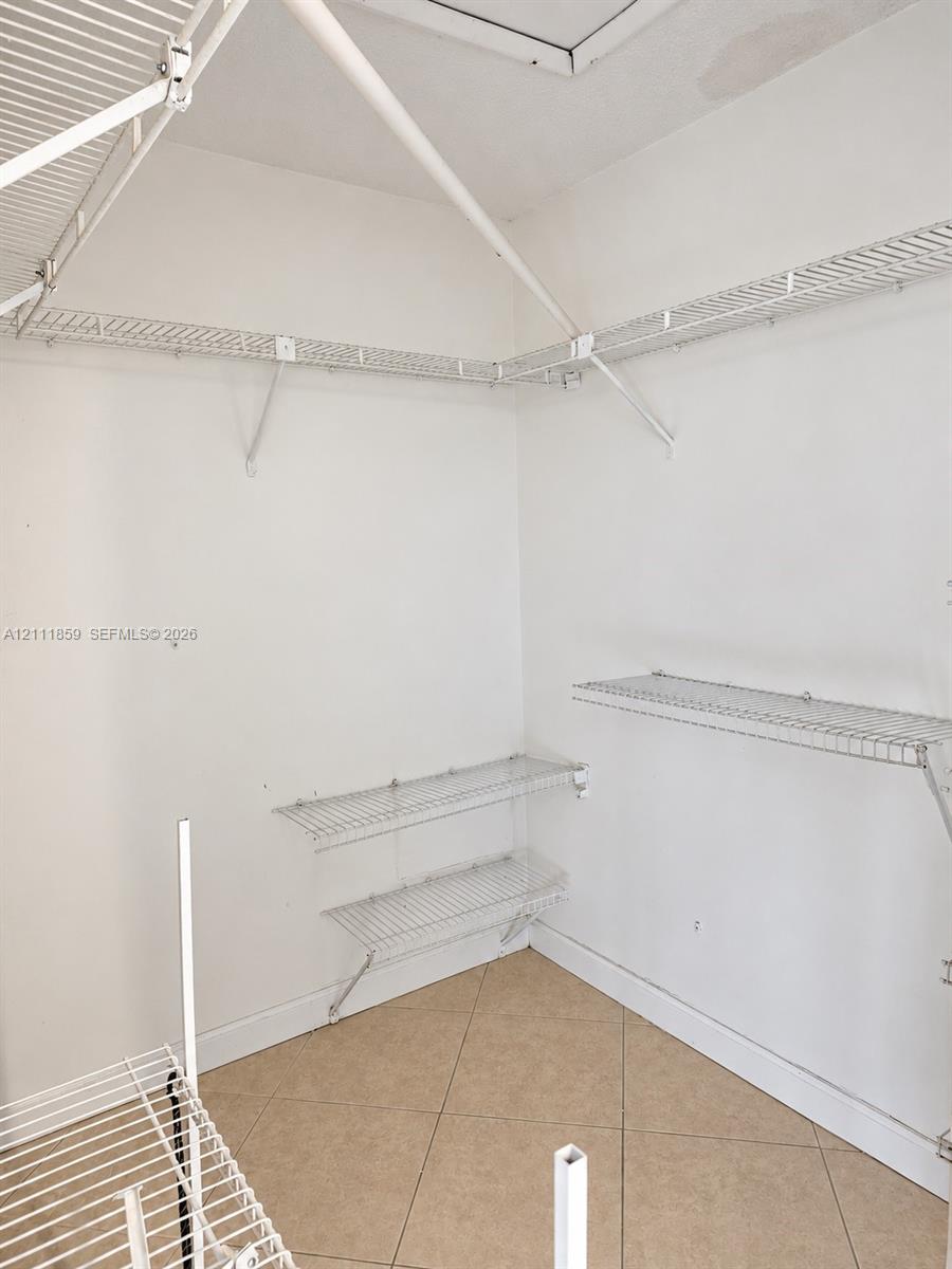 Storage space featuring white wire shelving units and neutral tile flooring