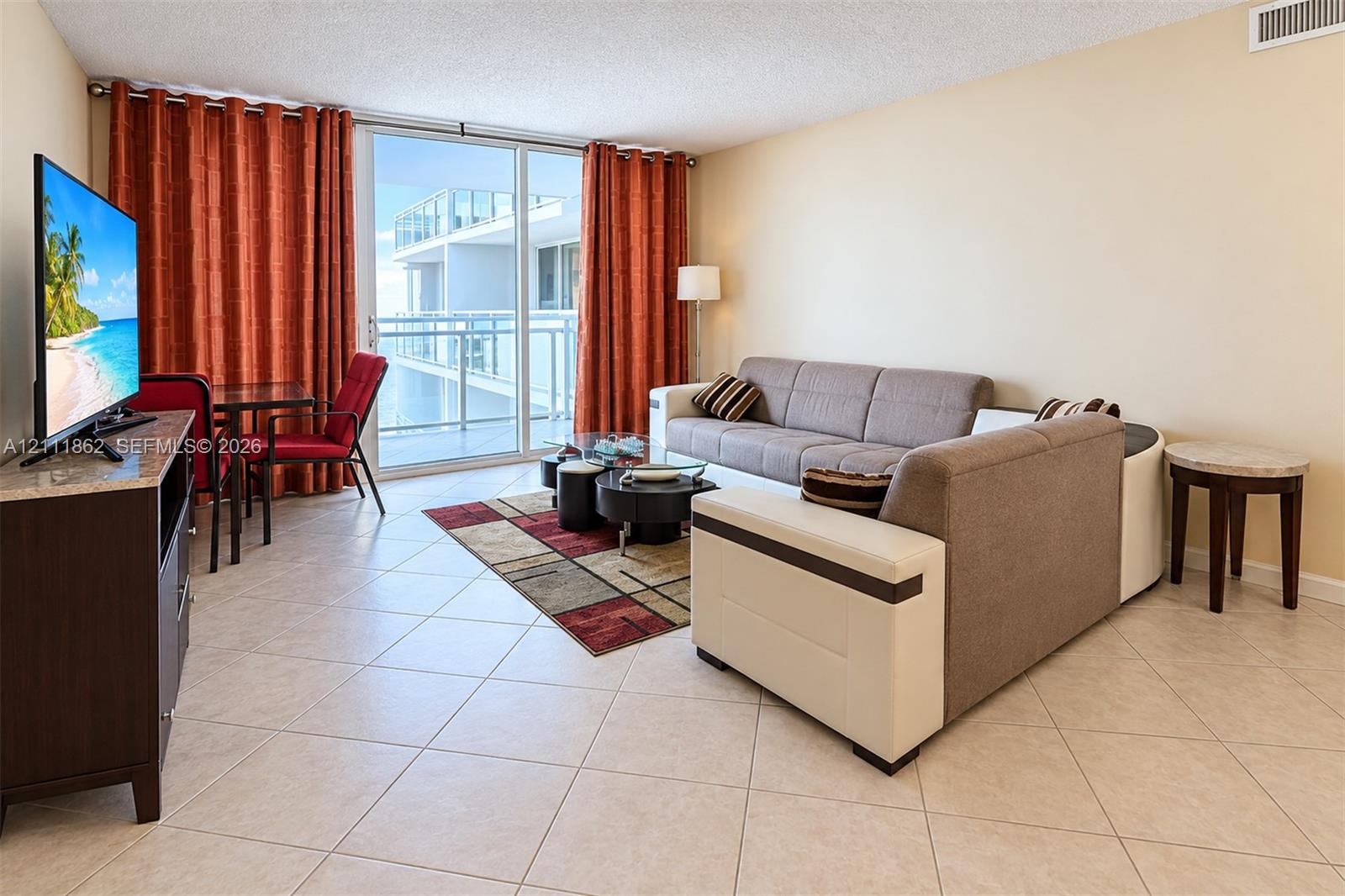 Living area featuring large-format diagonal tile flooring, floor-to-ceiling glass sliding doors, and a private balcony with metal railing