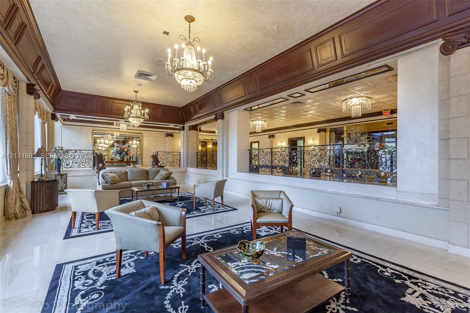 Expansive interior featuring high-gloss stone flooring, ornate crystal chandeliers, intricate dark wood crown molding, and decorative wrought-iron railings