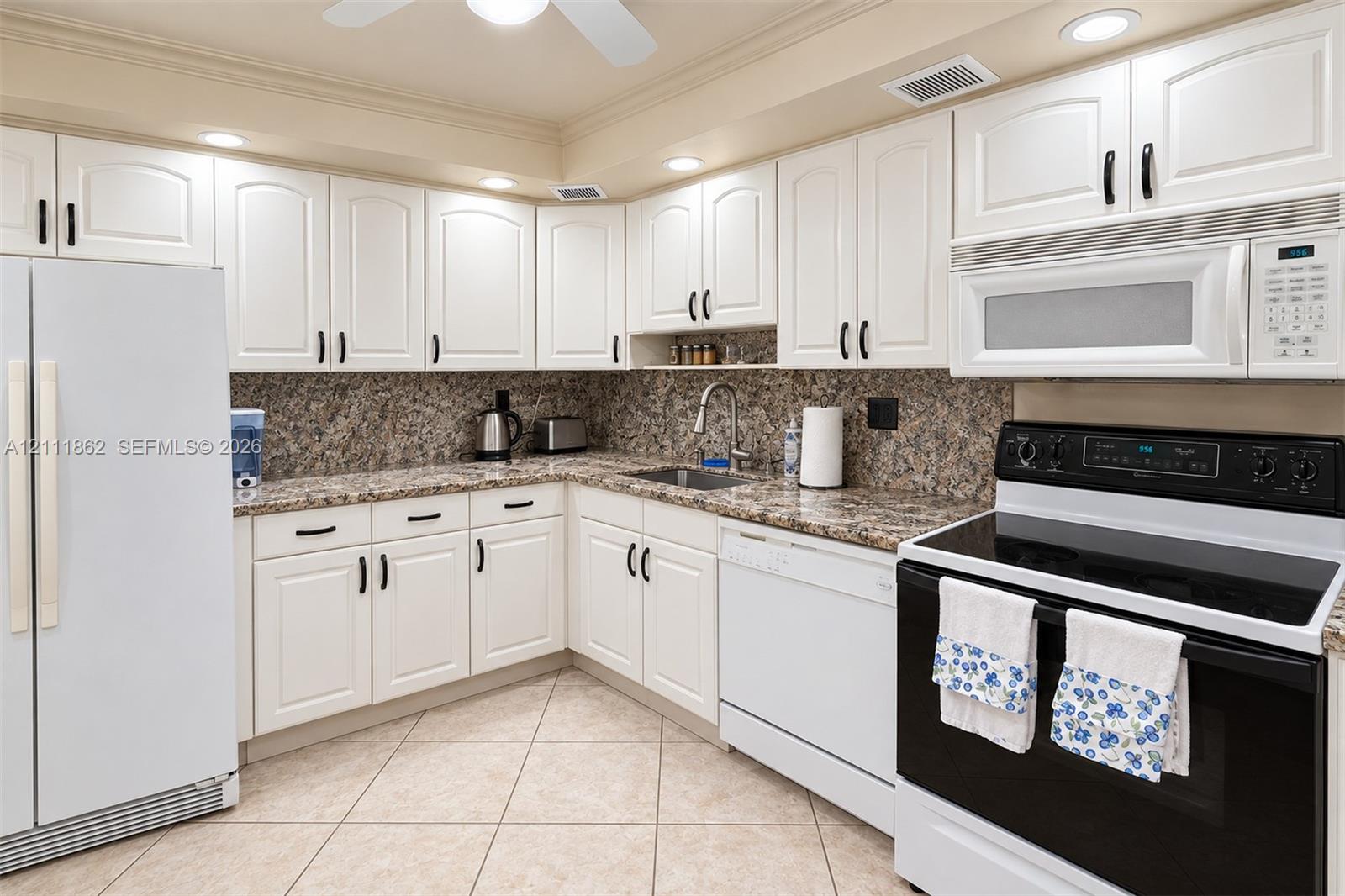 Kitchen featuring white shaker-style cabinetry, stone-finish countertops, tile flooring, recessed lighting, and a stainless steel arched faucet