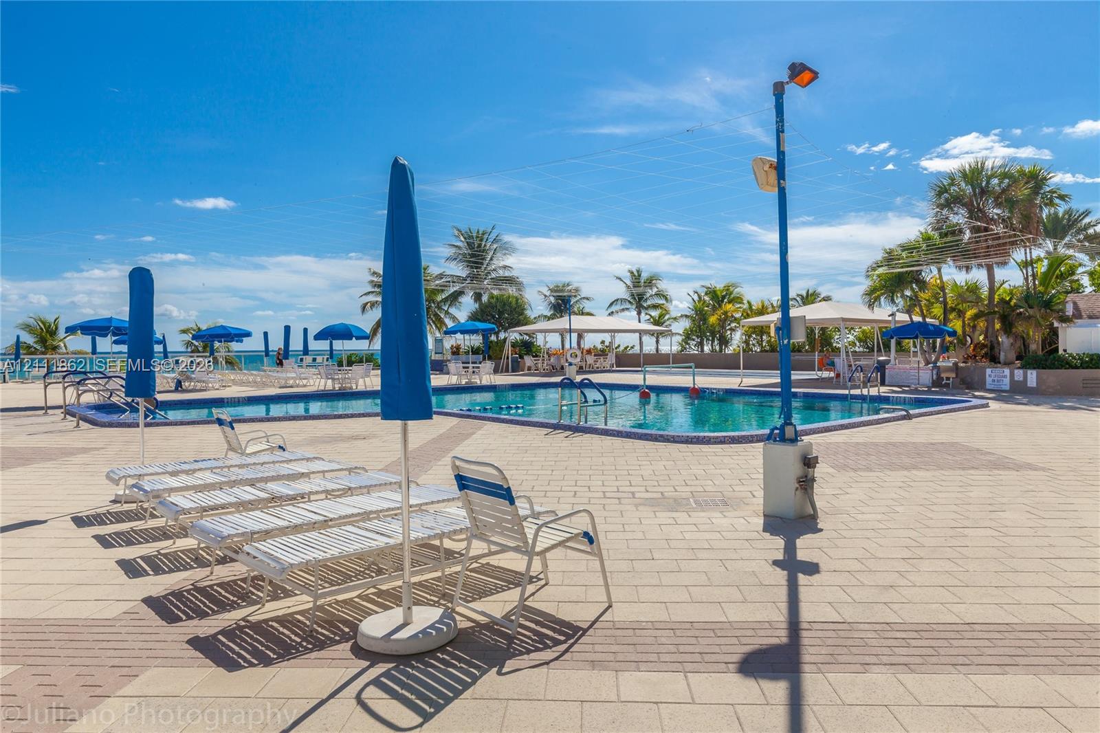 Outdoor swimming pool with tile surround, paved decking, and covered patio structures