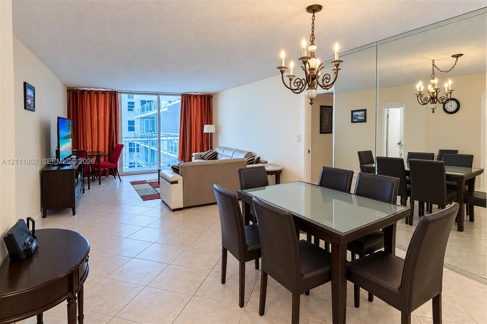 Open-concept floor plan featuring tile flooring, a floor-to-ceiling mirrored wall, iron-style chandelier, and glass balcony door
