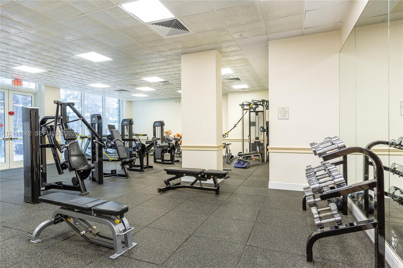 Fitness center featuring rubber flooring, floor-to-ceiling mirrored walls, recessed ceiling lighting, and expansive glass paneled doors