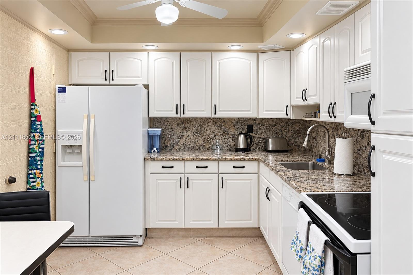 Kitchen featuring white raised-panel cabinetry, stone-patterned countertops, a stainless steel undermount sink with a gooseneck faucet, tile flooring, and recessed ceiling lighting