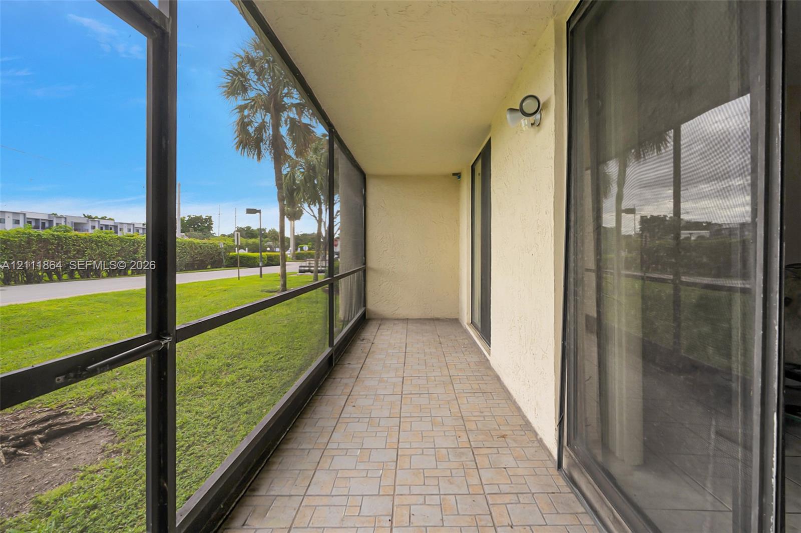 Screened-in porch featuring tile flooring, textured wall finishes, and an attached exterior light fixture