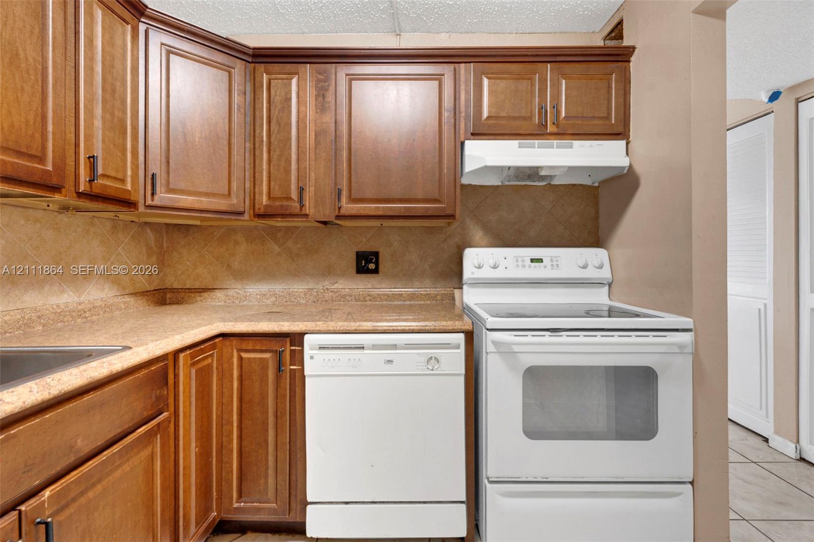 Kitchen featuring wood cabinetry, stone-finish countertops, tile backsplash, built-in dishwasher, and a freestanding electric range