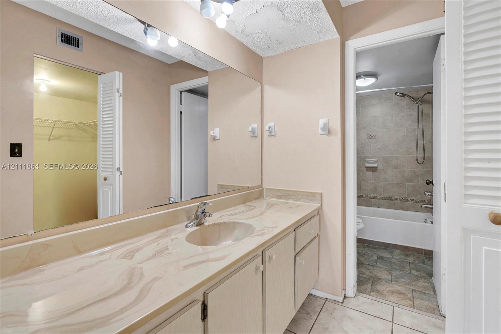 Bathroom vanity featuring a solid surface countertop with integrated basin, full-width wall mirror, wood-finish cabinetry, and tiled flooring