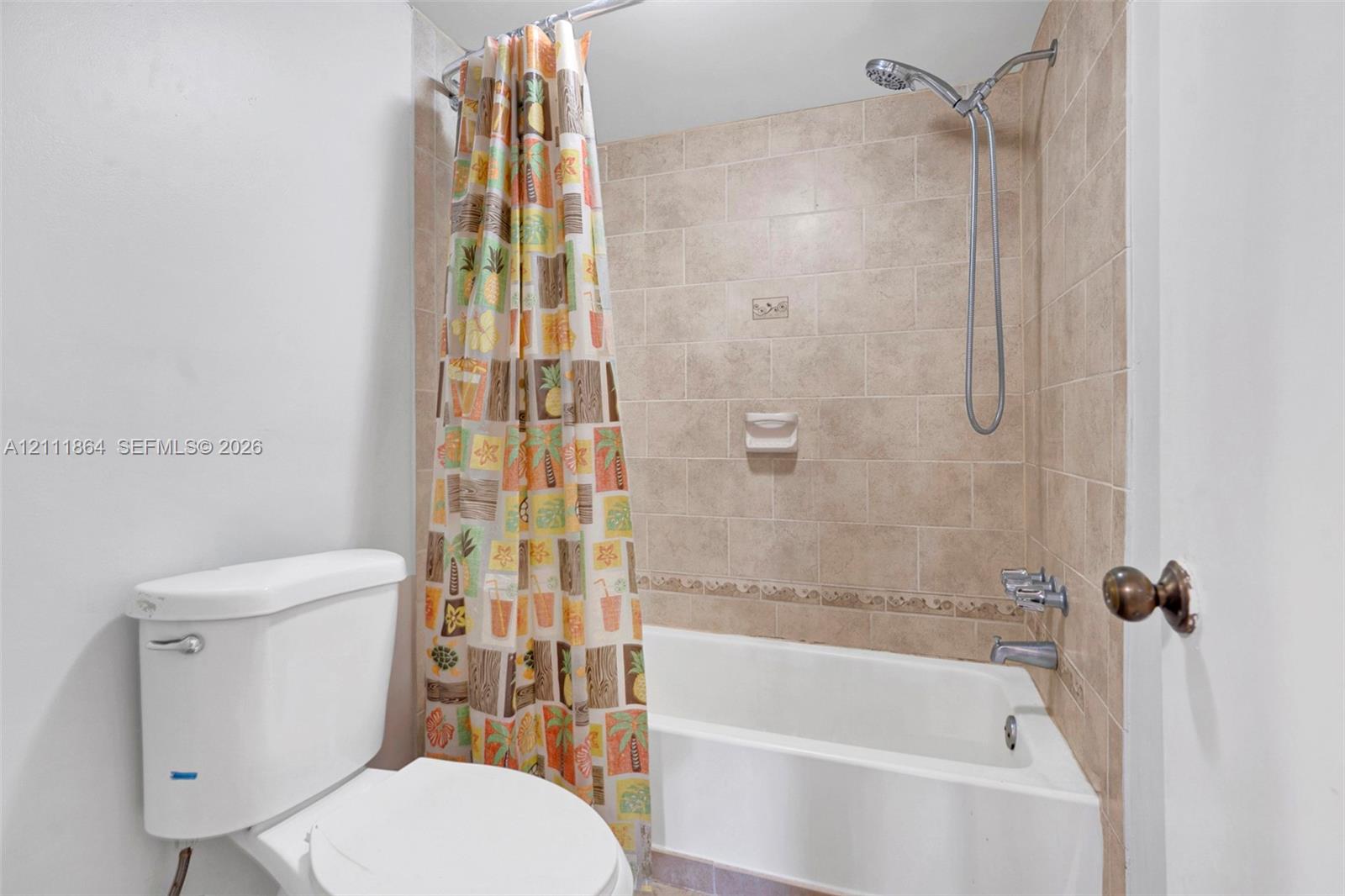 Bathroom featuring a porcelain tub, beige tile surround with a decorative inlay, a wall-mounted soap dish, and a chrome hand-held shower fixture