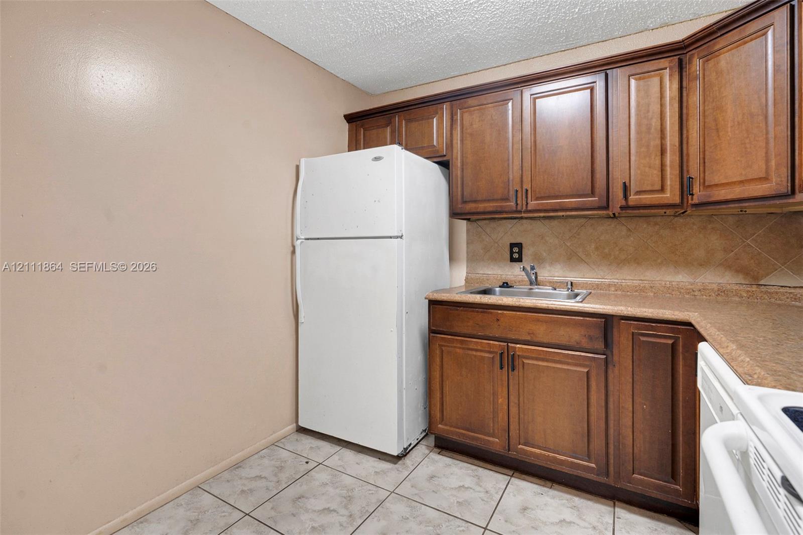 Kitchenette featuring wood cabinetry, solid surface countertops, tile backsplash, stainless steel sink, and ceramic tile flooring