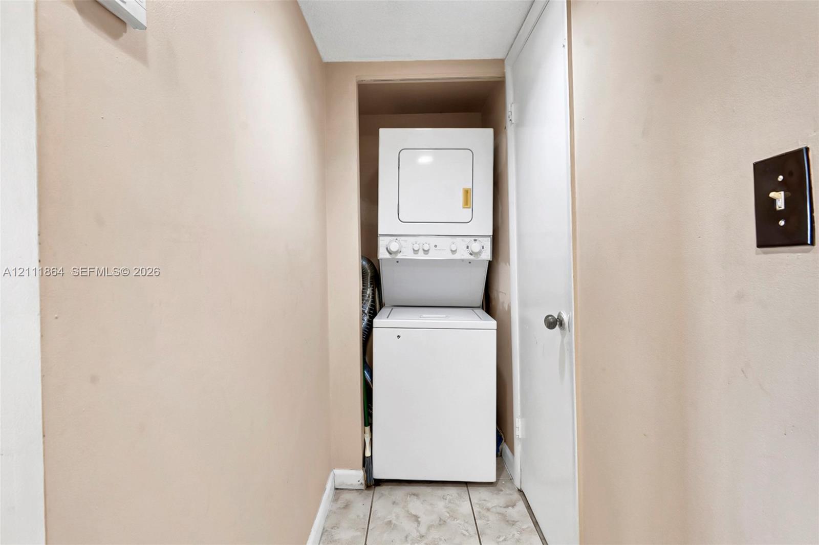 Utility closet featuring a stacked washer and dryer unit and tile flooring