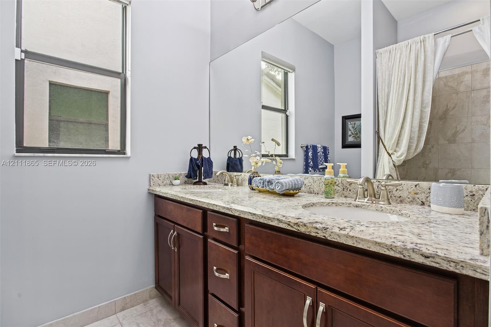 Second bathroom featuring a dual-sink vanity with stone countertops, rich wood-finish cabinetry & large wall-mounted mirror.