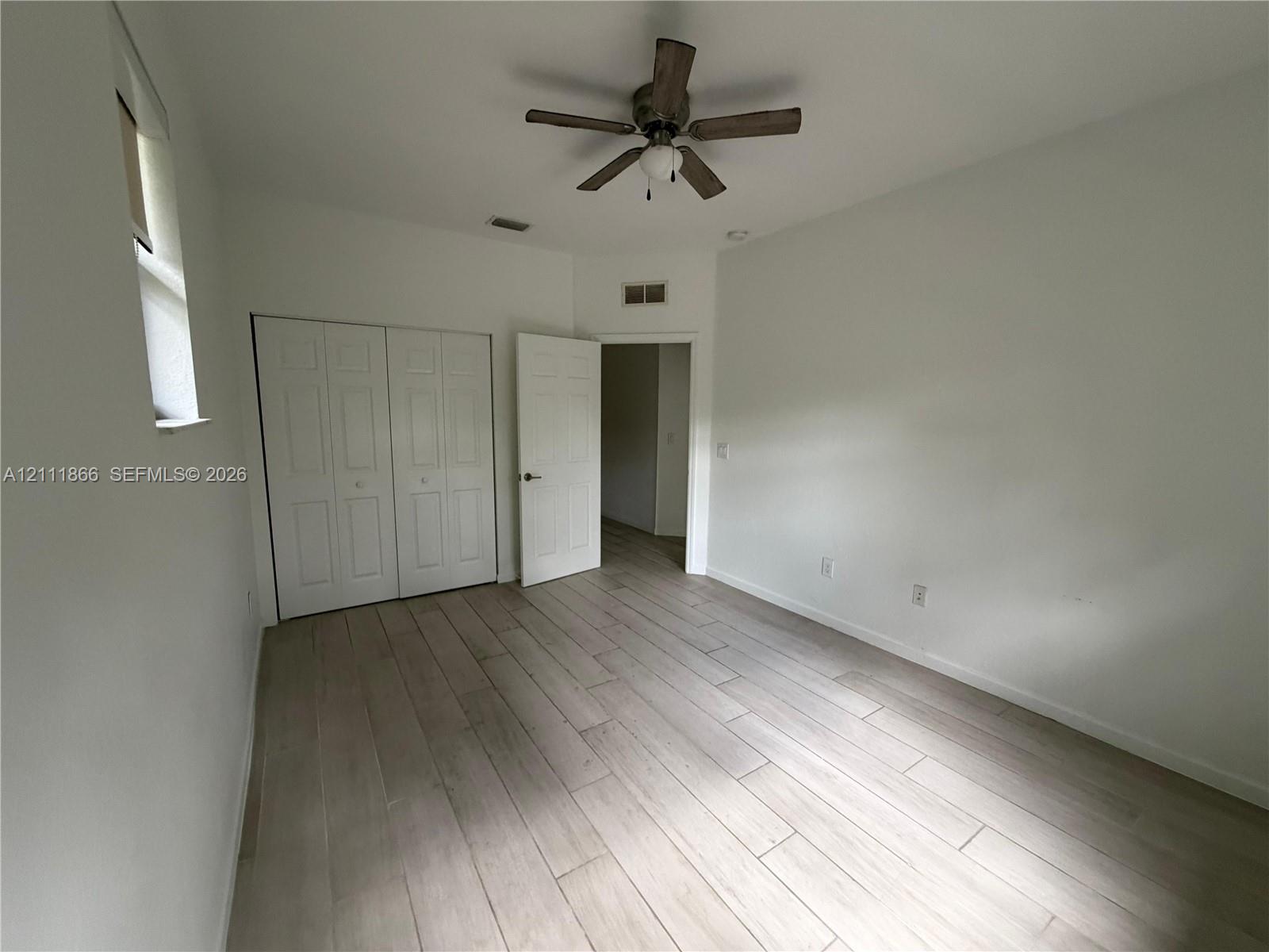 Interior room featuring wood-finish flooring, a ceiling fan with integrated light, a dual-panel closet door, and a single-panel interior door
