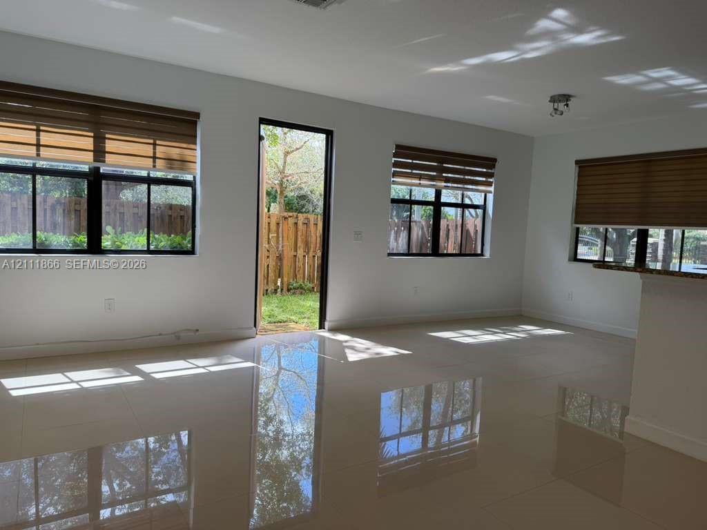 Interior space featuring large-format tile flooring, multiple windows with integrated blinds, and an exterior door providing access to a fenced yard