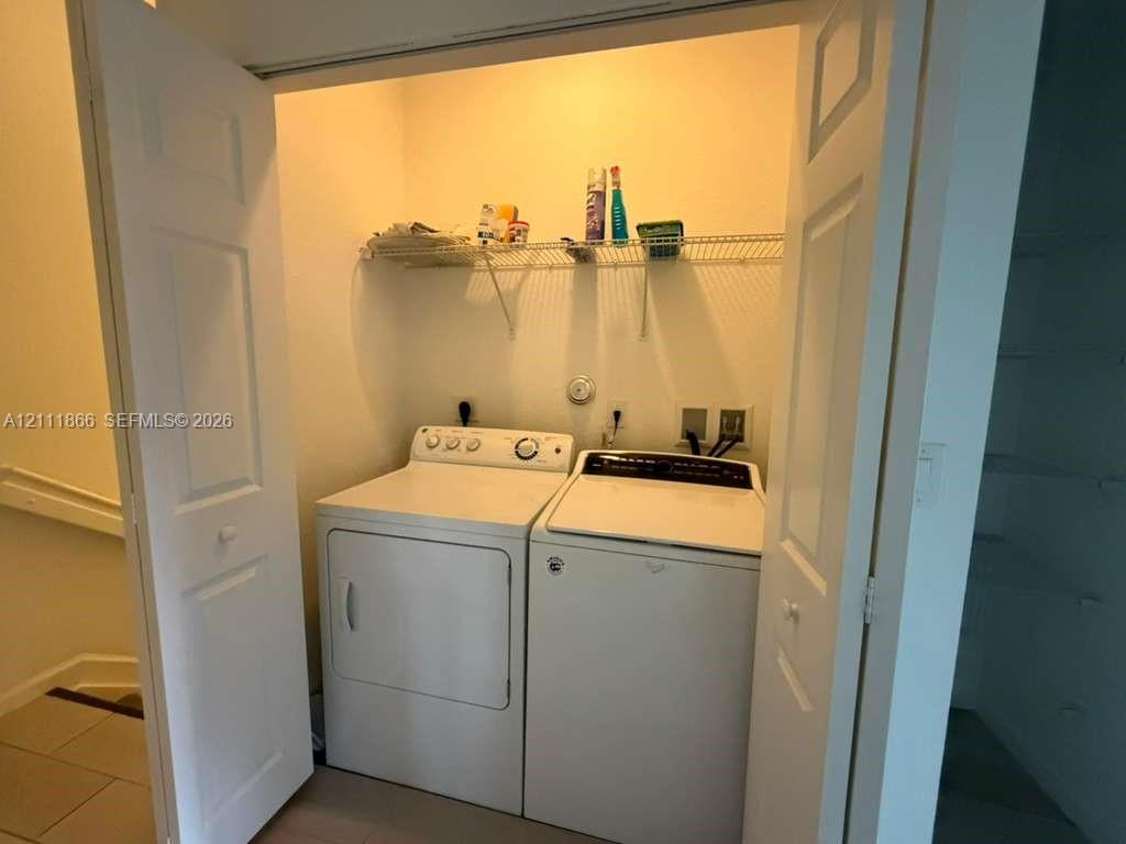 Laundry closet featuring a pair of white appliances and a wire-rack storage shelf, enclosed by double paneled doors