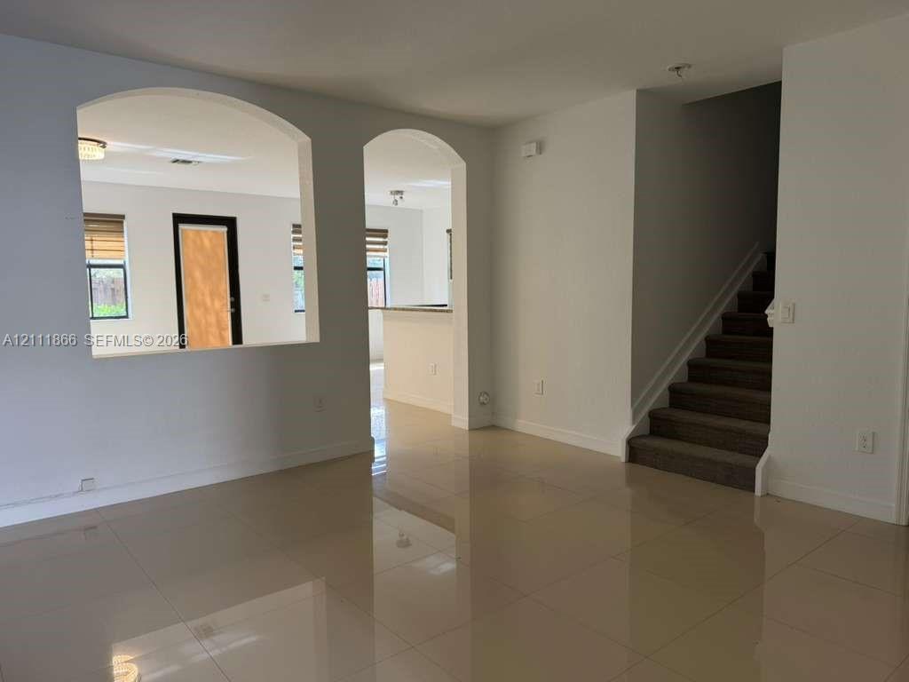 Interior featuring arched architectural pass-throughs, large-format tile flooring, and carpeted staircase