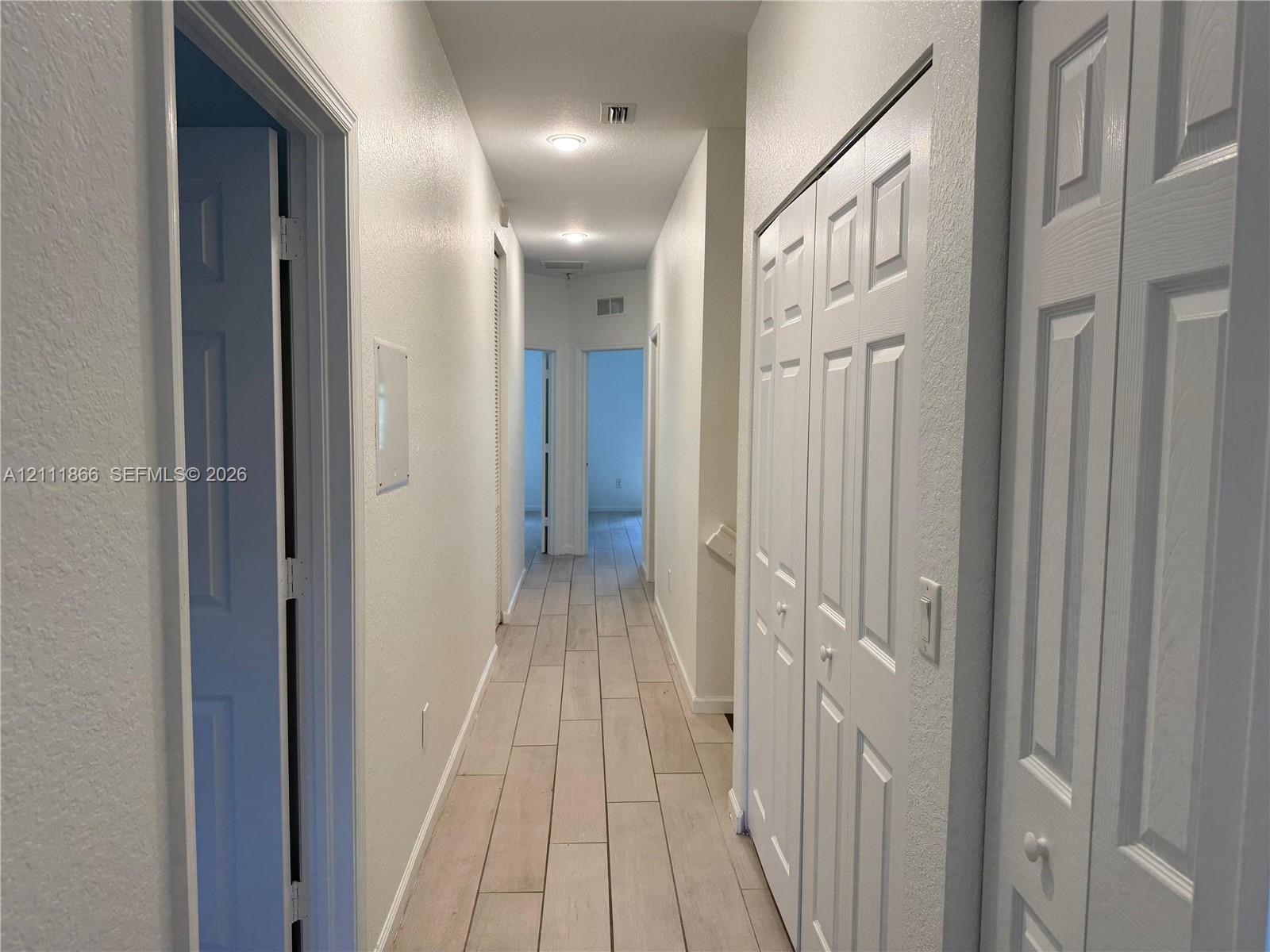 Hallway featuring wood-finish flooring, recessed ceiling lighting, and multiple bi-fold closet doors