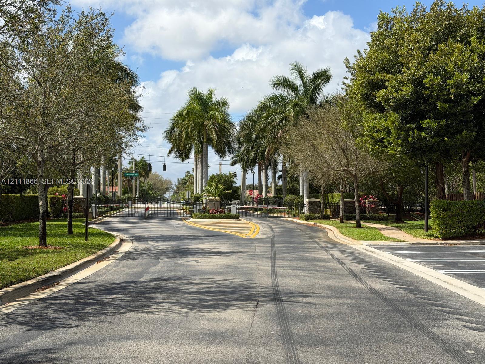 Gated entrance featuring tall palm trees, mature landscaping, and manicured lawns