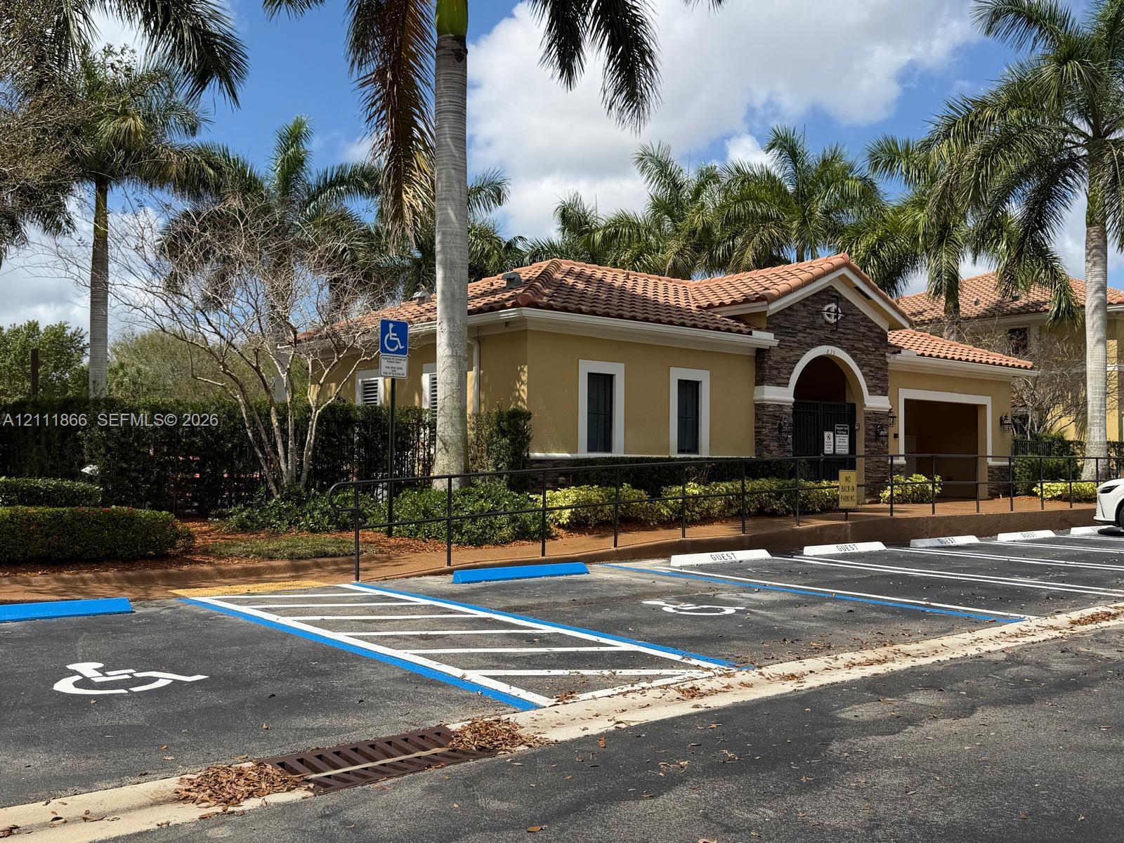 Stucco exterior featuring stone veneer accents, terra-cotta tile roofing, arched entryway, and landscaped grounds with mature palm trees
