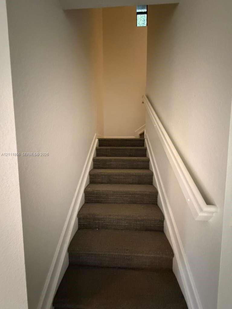Staircase featuring textured carpeted treads and a mounted white handrail