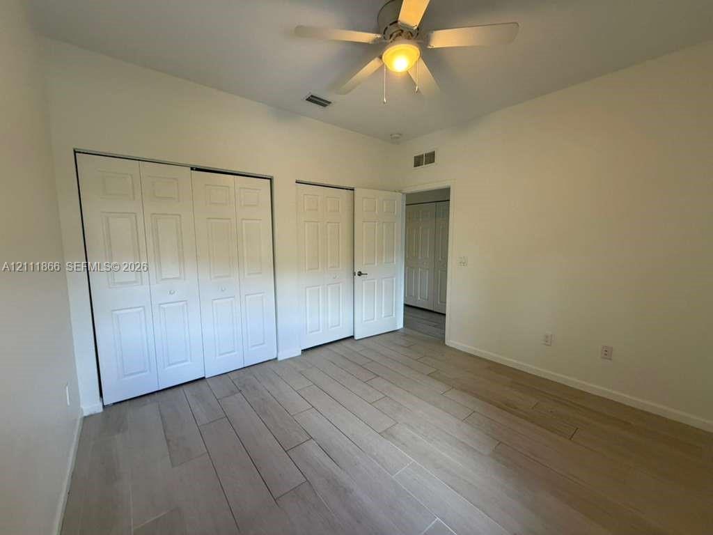 Room featuring wood-finish flooring, dual-door closet storage, and a ceiling fan with integrated lighting