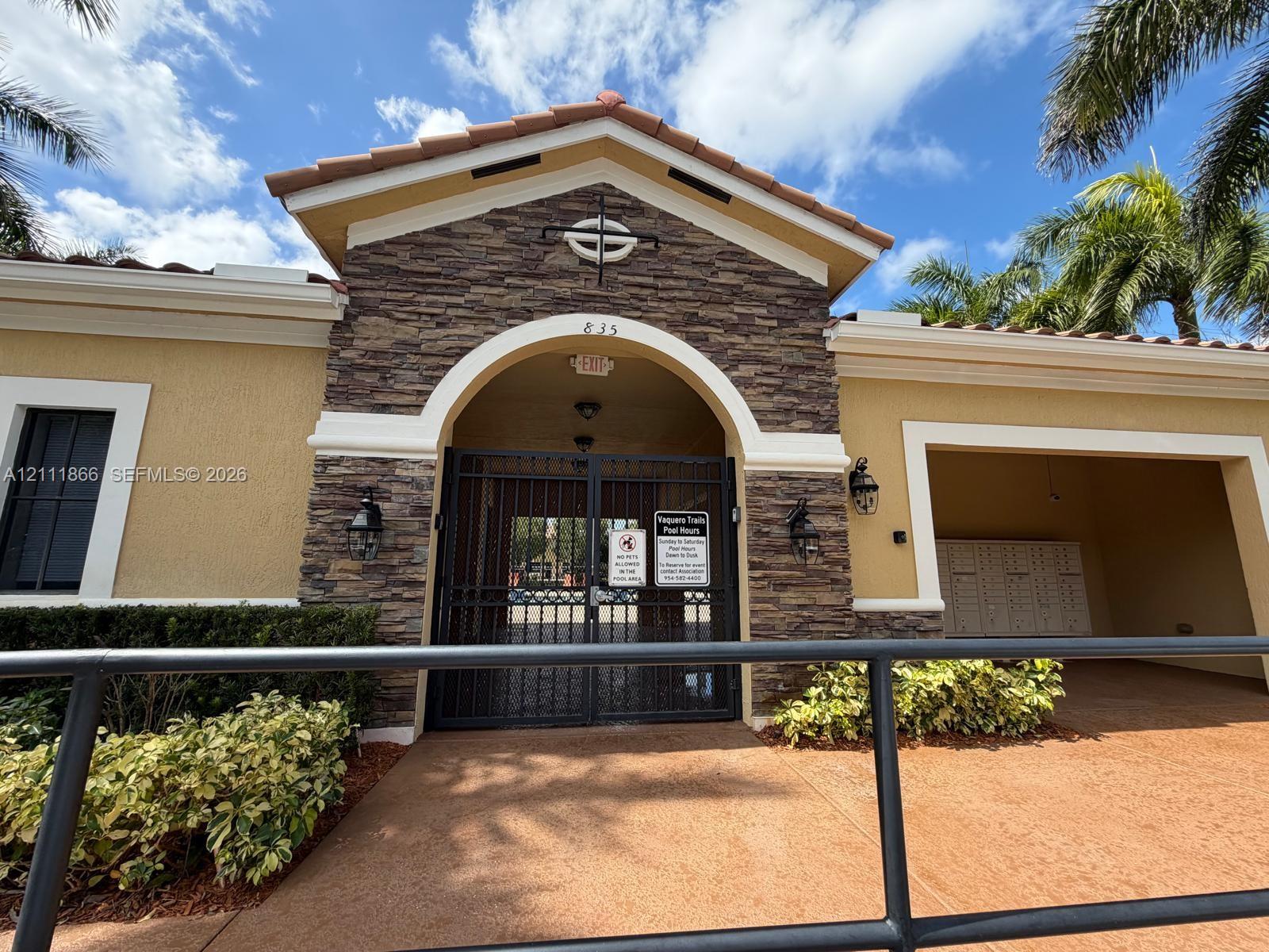 Stone-veneer facade featuring a tiled gable roof, arched entry with decorative iron gates, and integrated outdoor lighting fixtures