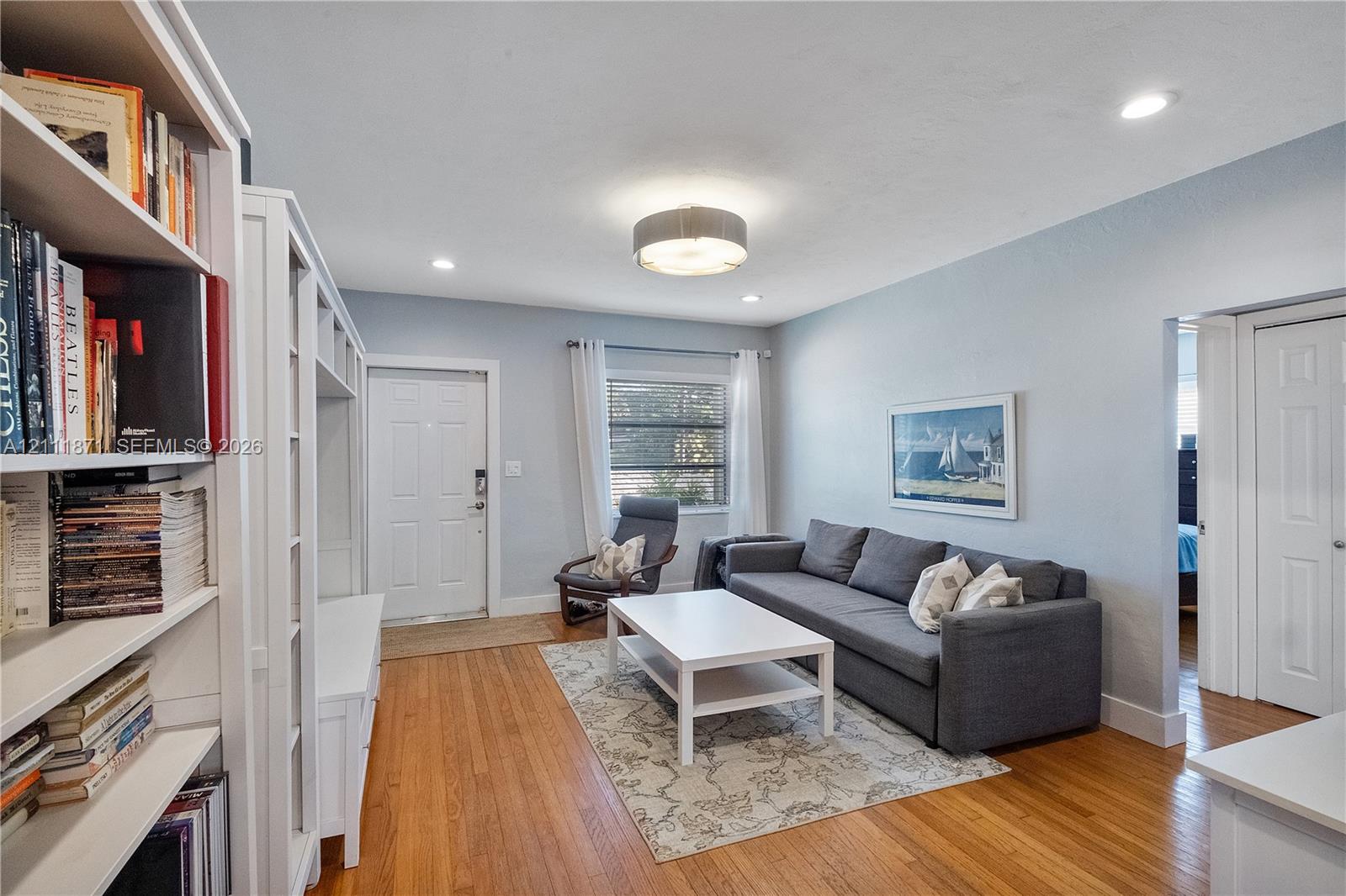Living area featuring wood-finish flooring, built-in floor-to-ceiling shelving, recessed lighting, and a drum-style ceiling fixture