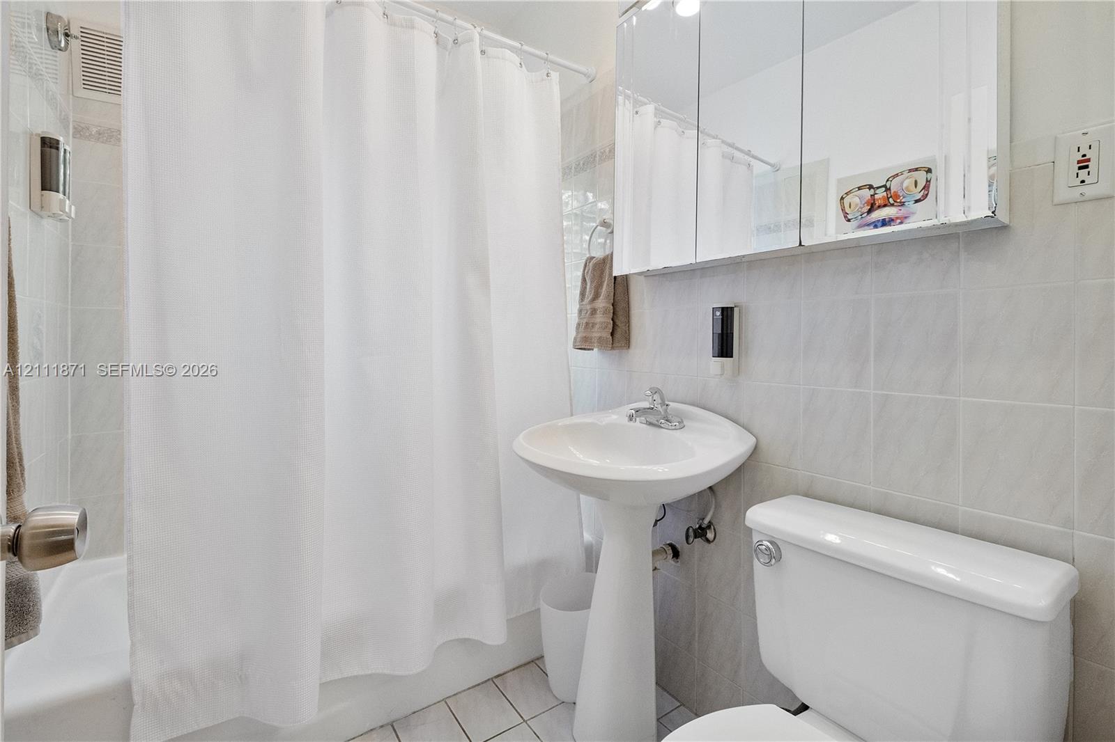 Bathroom featuring a pedestal sink, white tile wall surround, tub-shower combination, and a mirrored medicine cabinet