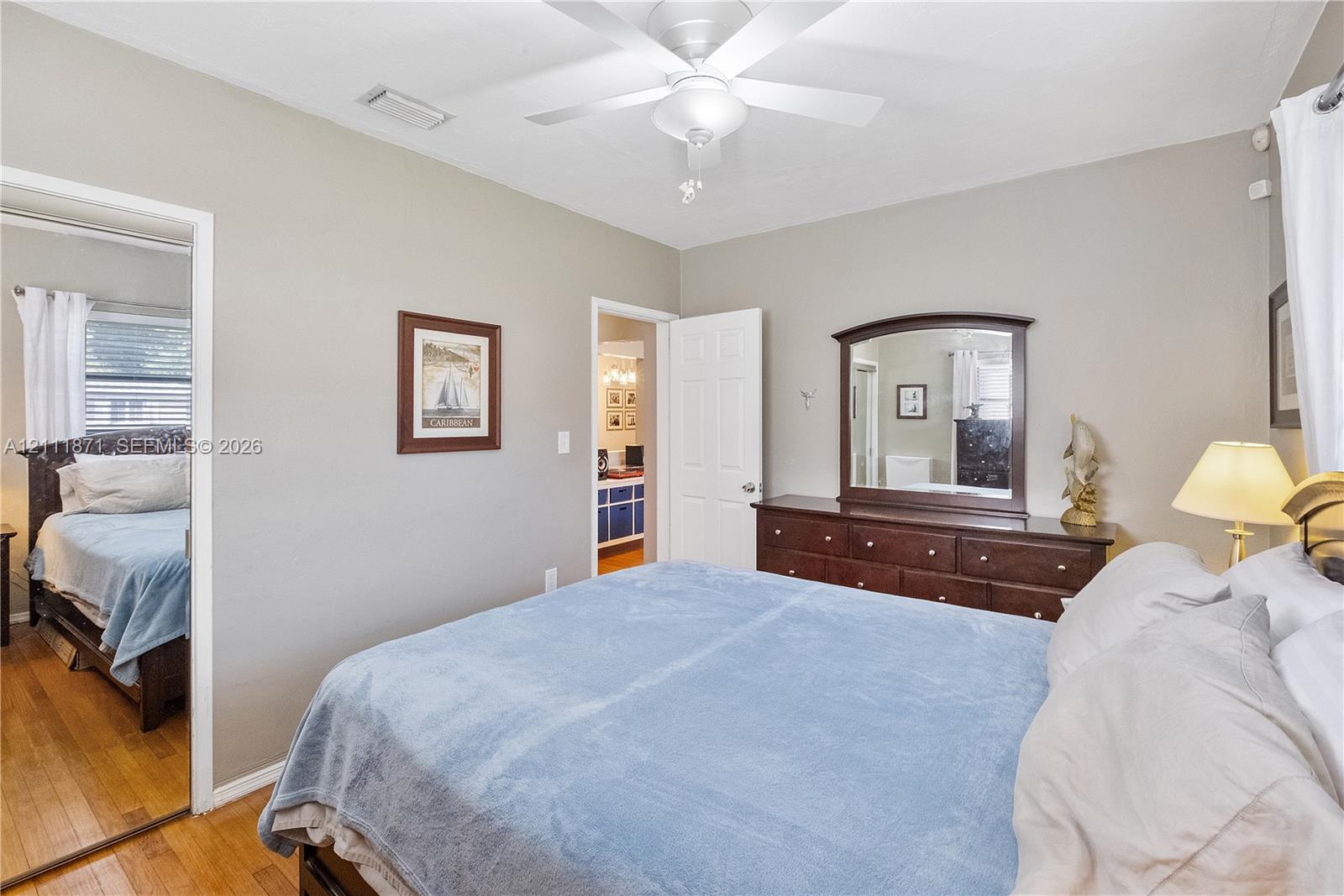 Room featuring wood-finish flooring, a white ceiling fan with integrated lighting, and a multi-panel interior door