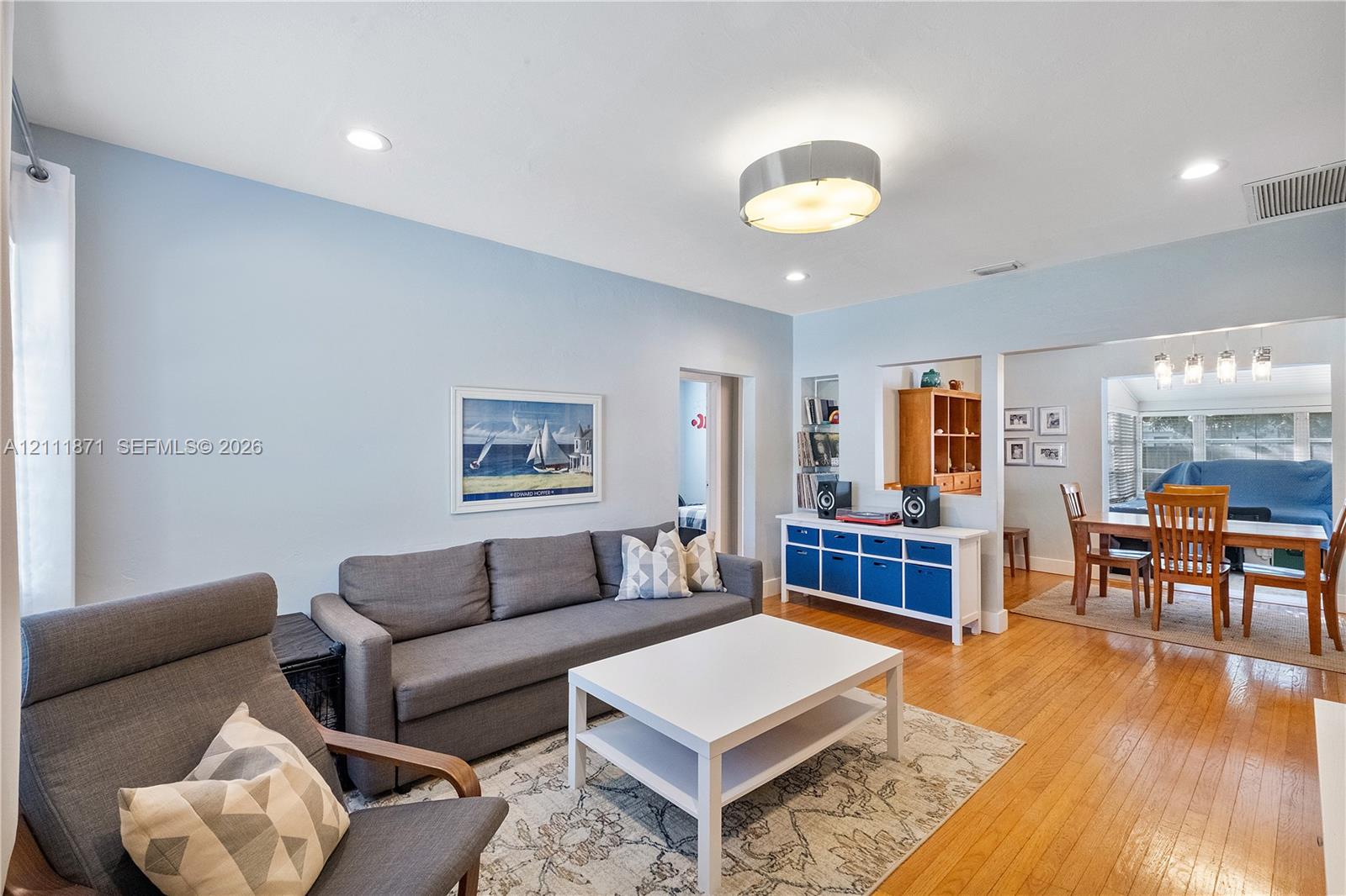 Living area featuring wood-finish flooring, recessed lighting, a central drum-style ceiling fixture, and a built-in display niche with shelving