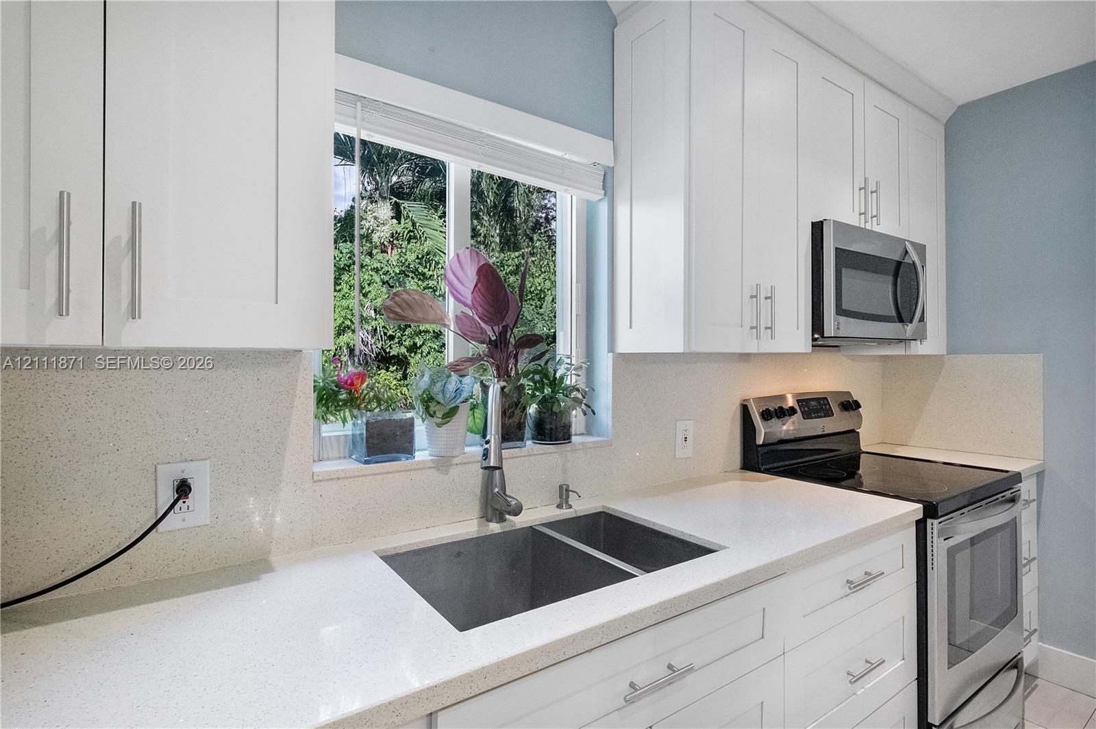Kitchen featuring white shaker-style cabinetry, solid-surface countertops, dual-basin stainless steel sink with high-arc faucet, and stainless steel appliances