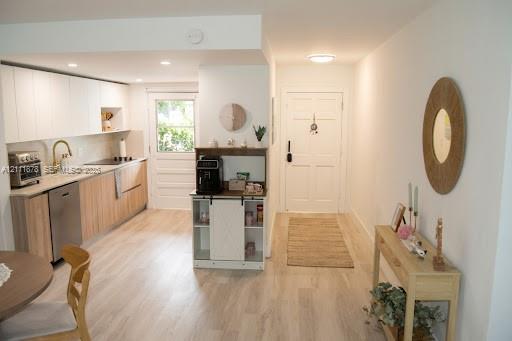 Kitchen featuring flat-panel upper cabinetry, wood-finish lower cabinetry, integrated stainless steel dishwasher, gold-tone hardware, and wood-finish flooring